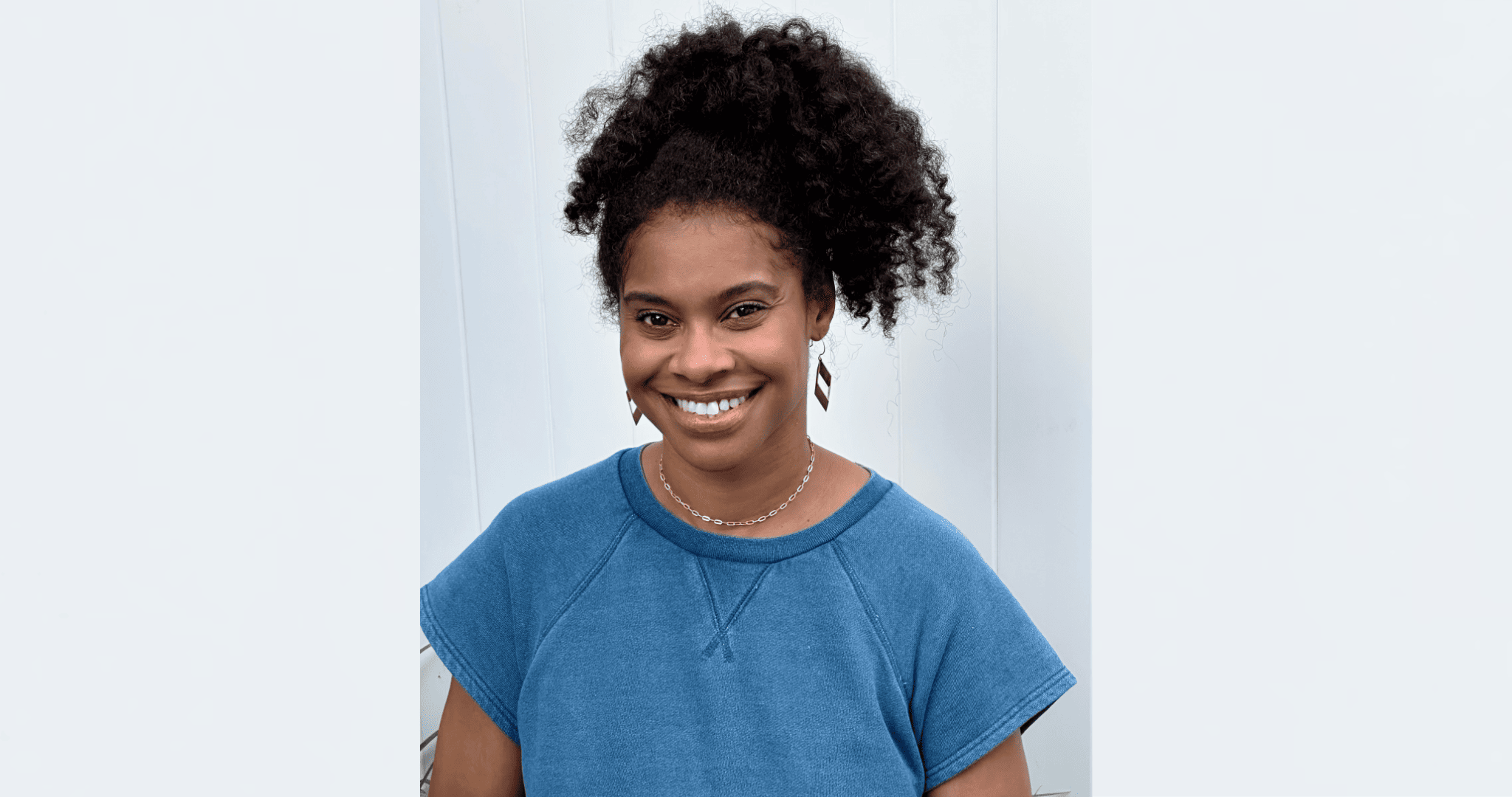 A woman with curly hair and a blue shirt smiling warmly.