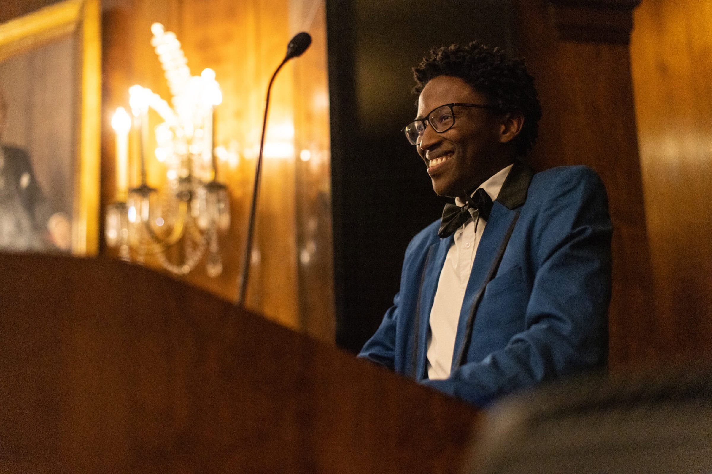 A student in business attire smiles at the audience behind a podium with a mic at Senior Dinner.